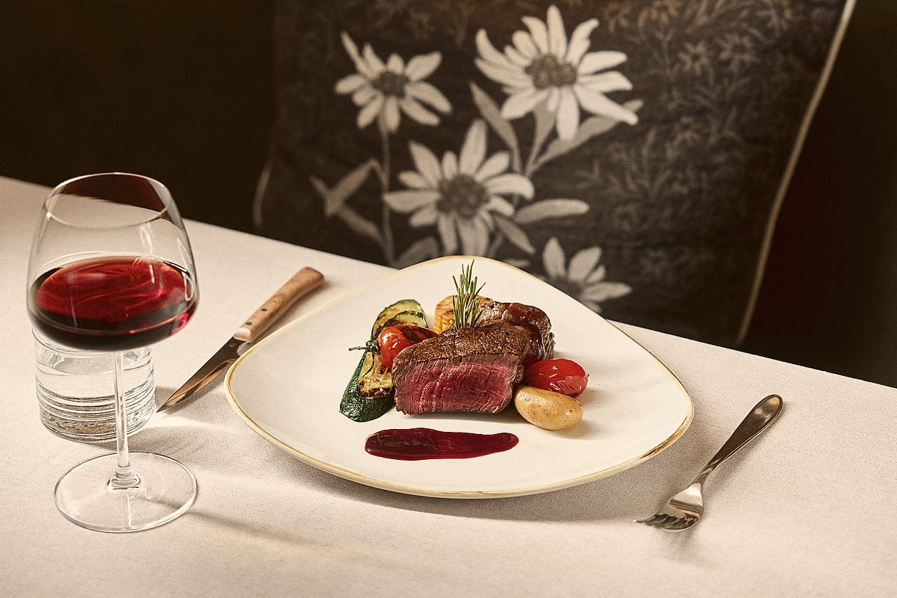 Gegrilltes Filet mit Gemüse und einem Glas Rotwein auf weißem Tischtuch
